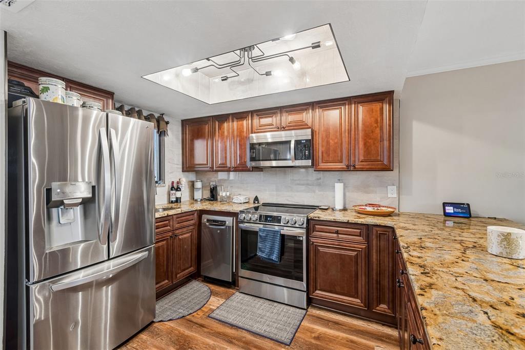 A kitchen features dark wood cabinets, granite countertops, stainless steel appliances, and a recessed light fixture — 6009 SEA RANCH DRIVE UNIT 503, HUDSON, FL