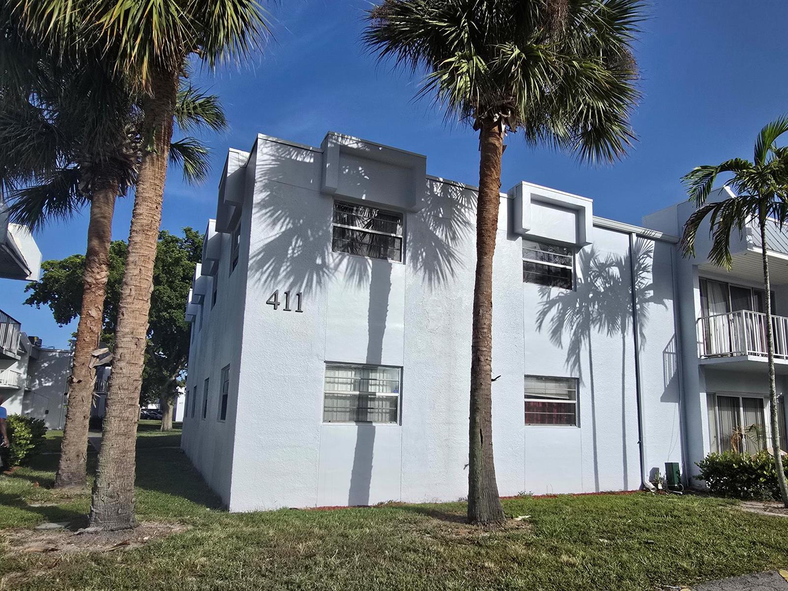 A two-story light blue apartment building with palm trees and the number 411 displayed — 411 Executive Center Drive # 210, West Palm Beach FL 33401, WEST PALM BEACH, FL