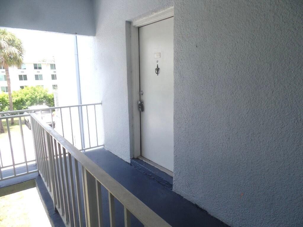 A white apartment door with a peephole and lock is located on an outdoor balcony — 411 Executive Center Drive # 210, West Palm Beach FL 33401, WEST PALM BEACH, FL