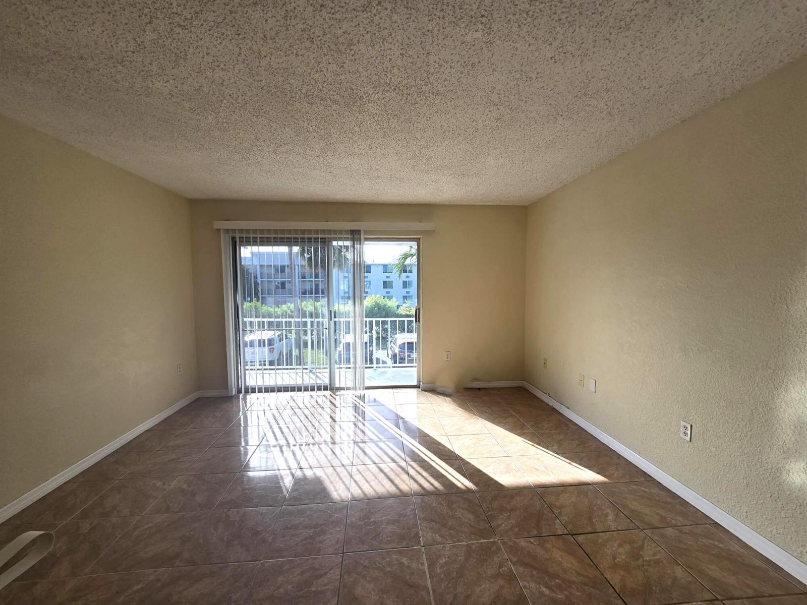 An empty room with beige walls, tile flooring, and a sliding glass door to a balcony — 411 Executive Center Drive # 210, West Palm Beach FL 33401, WEST PALM BEACH, FL