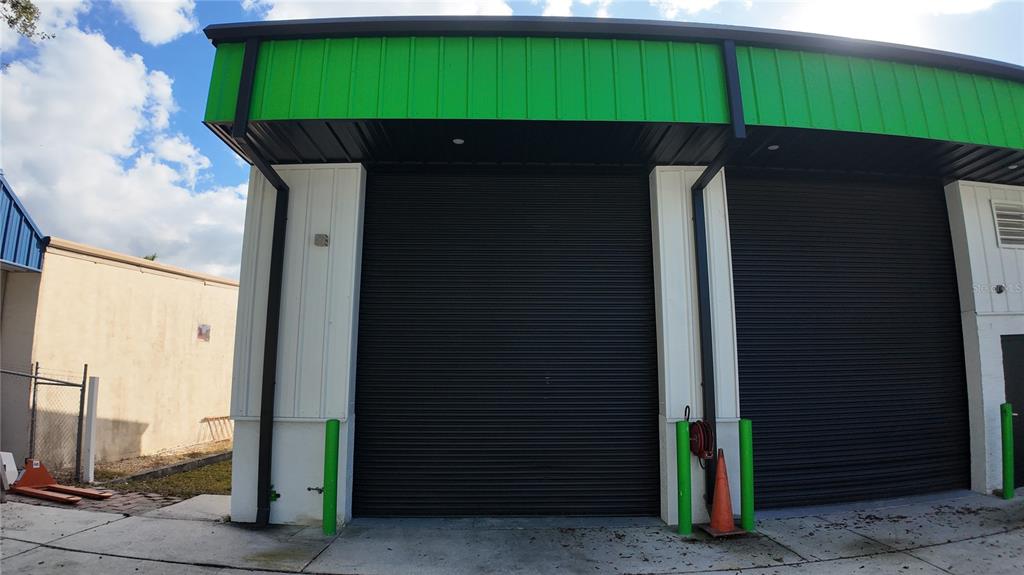 Exterior view of a commercial building featuring two black roll-up doors and green trim — 2024 PRINCETON STREET, SARASOTA, FL