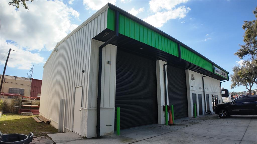 A commercial building with white metal siding, green trim, and two large black roll-up doors — 2024 PRINCETON STREET, SARASOTA, FL