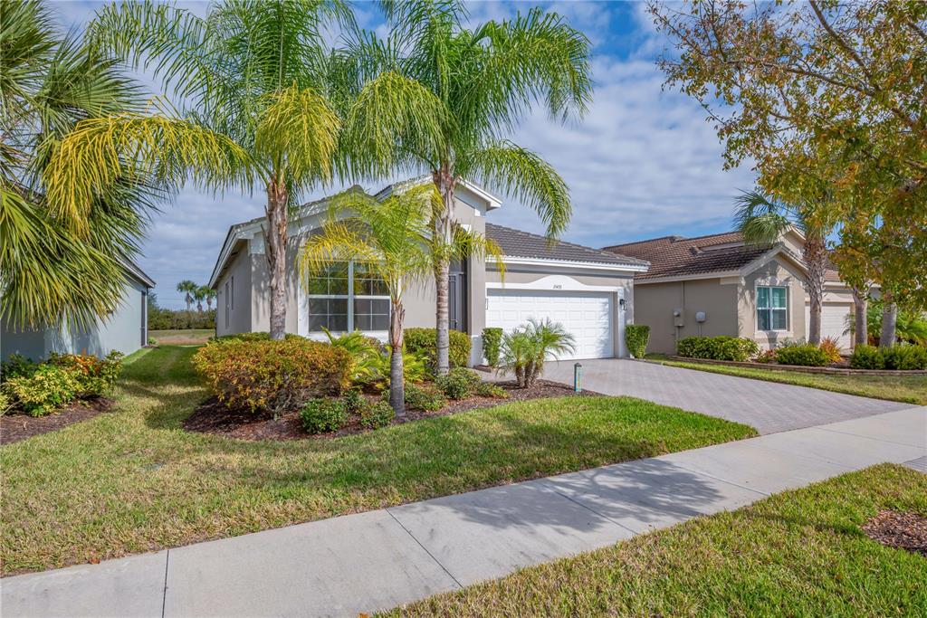 A single-story house with a paved driveway, palm trees, and a two-car garage — 15433 SANTA POLA DRIVE, WIMAUMA, FL