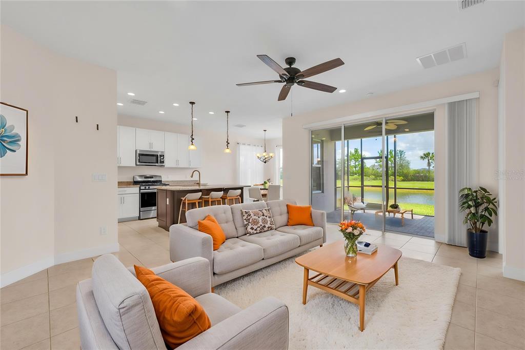 A living room with a sofa and armchair opens to a kitchen and a screened patio — 15433 SANTA POLA DRIVE, WIMAUMA, FL