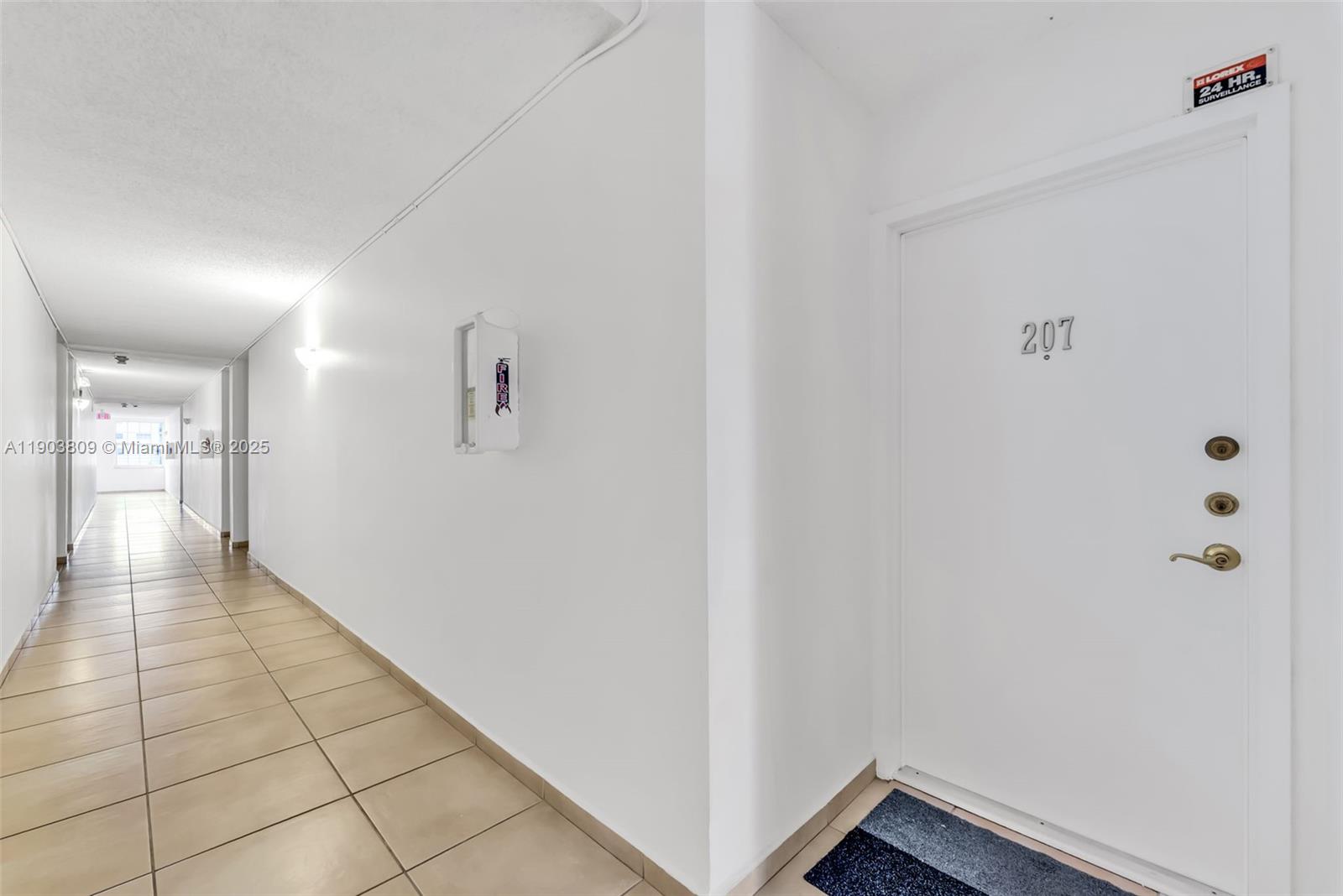 A white apartment hallway features tiled flooring, a fire extinguisher cabinet, and unit door 207 — 3661 SW 9th Ter # 207, Miami FL 33135, MIAMI, FL