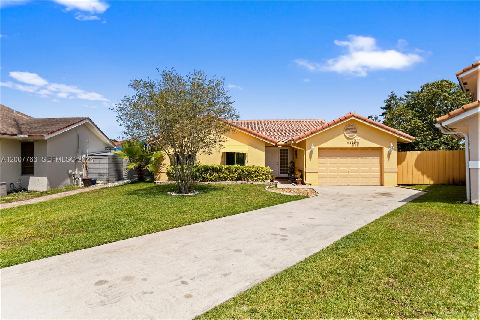 A single-story yellow house with a tiled roof and a concrete driveway sits under a blue sky — 6450 SW 13th St, Plantation FL 33317, PLANTATION, FL
