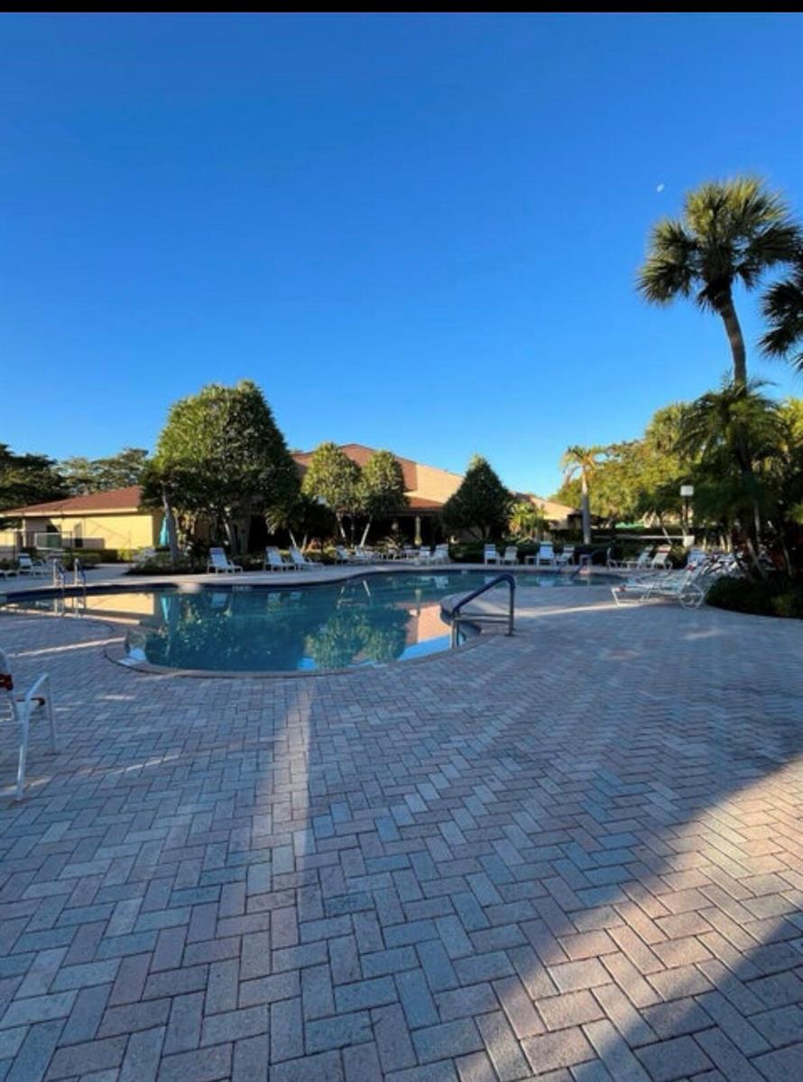 A swimming pool with a brick paver deck surrounded by palm trees and a building — 600 Egret Circle # 7305, Delray Beach FL 33444, DELRAY BEACH, FL