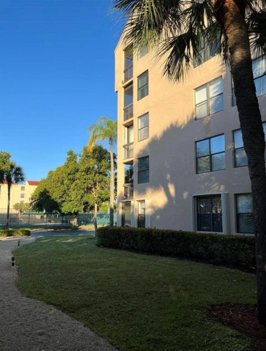 A multi-story beige apartment building stands next to a grassy lawn and palm trees — 600 Egret Circle # 7305, Delray Beach FL 33444, DELRAY BEACH, FL