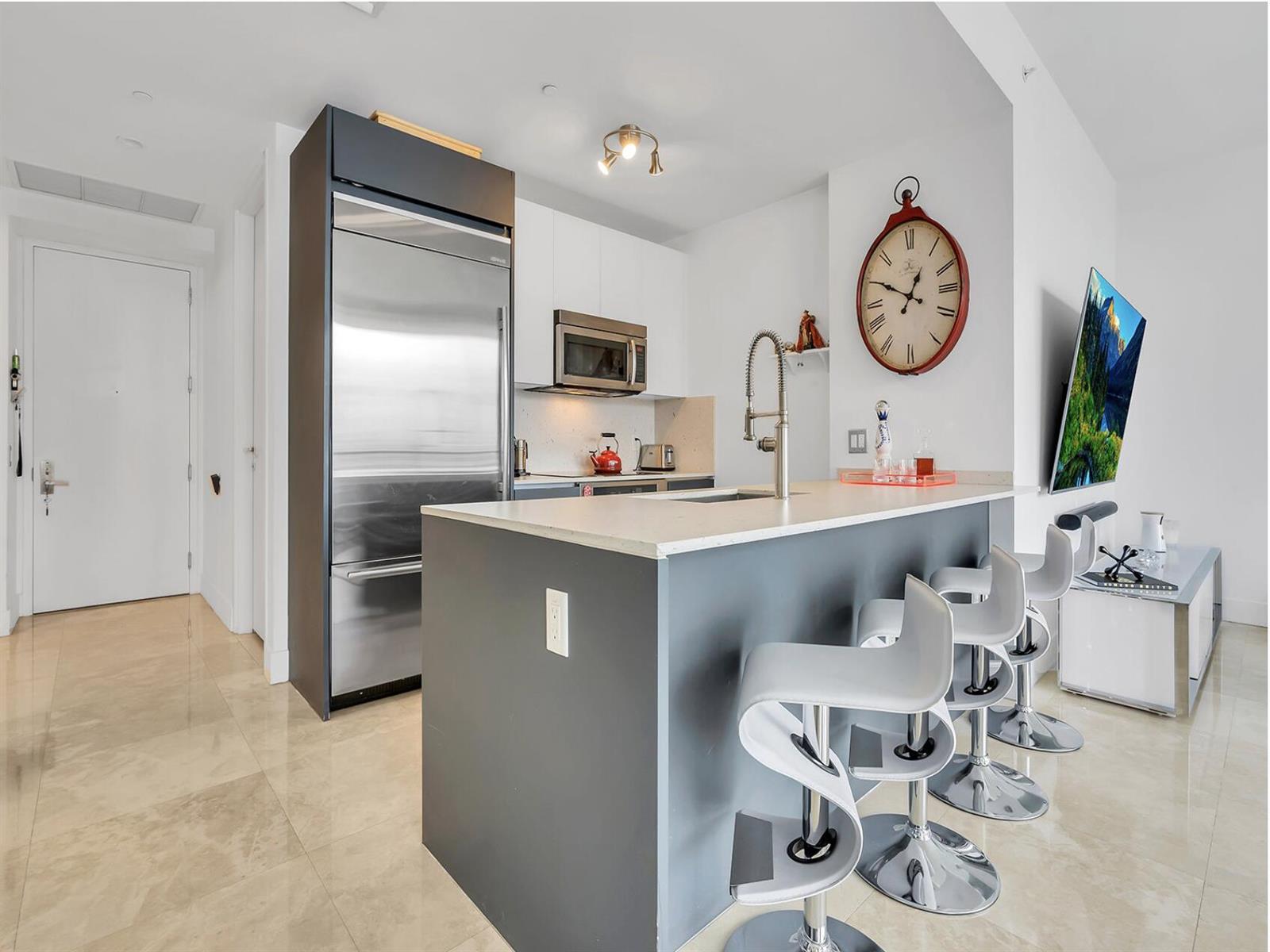 A modern kitchen features a gray island with bar stools, stainless steel appliances, and tile flooring — 1300 Brickell Bay Drive # 3900, Miami FL 33131, MIAMI, FL