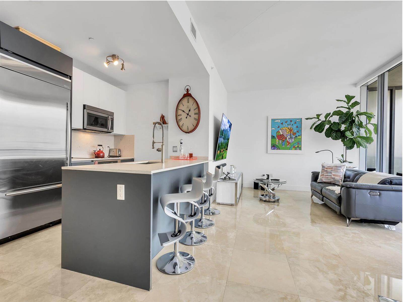A modern open-concept kitchen and living area with a breakfast bar, stainless appliances, and tile — 1300 Brickell Bay Drive # 3900, Miami FL 33131, MIAMI, FL