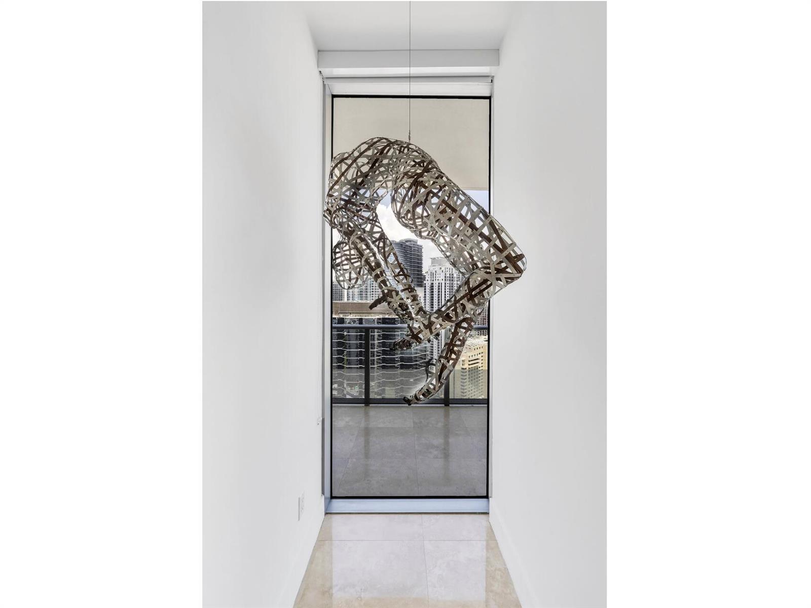A narrow hallway with white walls leads to a floor-to-ceiling window featuring a hanging sculpture — 1300 Brickell Bay Drive # 3900, Miami FL 33131, MIAMI, FL