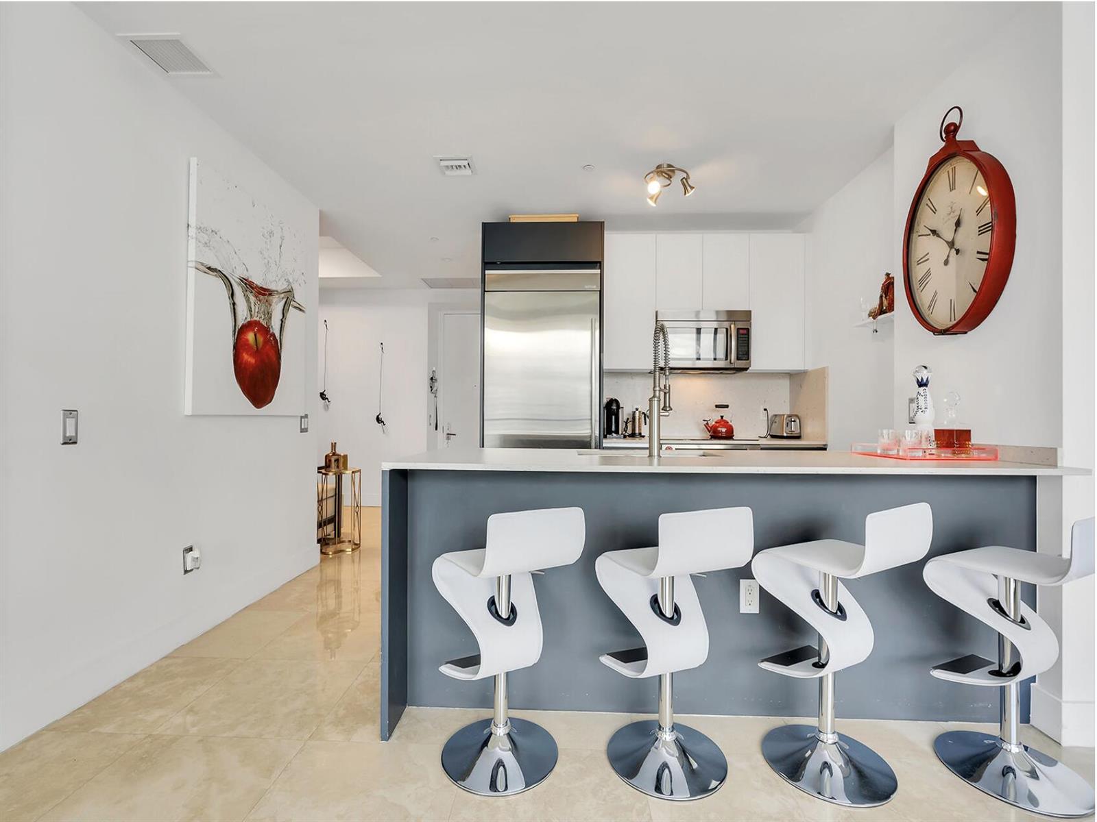 A modern kitchen features a gray breakfast bar with white stools and stainless steel appliances — 1300 Brickell Bay Drive # 3900, Miami FL 33131, MIAMI, FL
