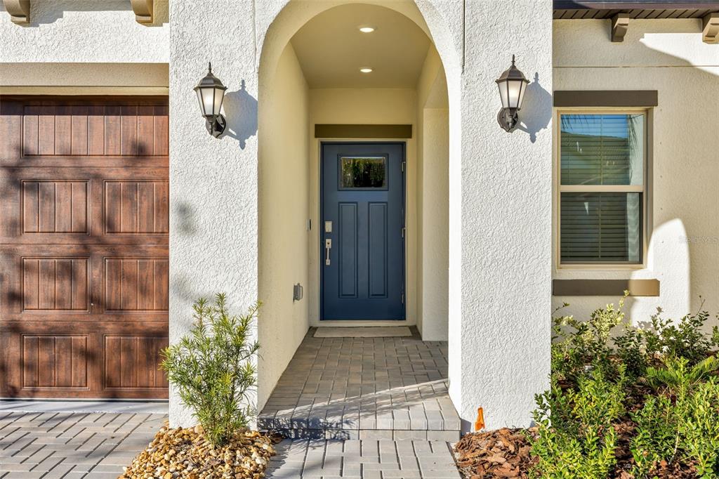 A blue front door is centered within an arched entryway next to a wood-paneled garage — 17523 HOLLY WELL AVENUE, WIMAUMA, FL