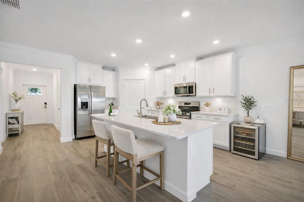 A modern kitchen features white cabinetry, a central island with bar seating, and stainless appliances — 17523 HOLLY WELL AVENUE, WIMAUMA, FL