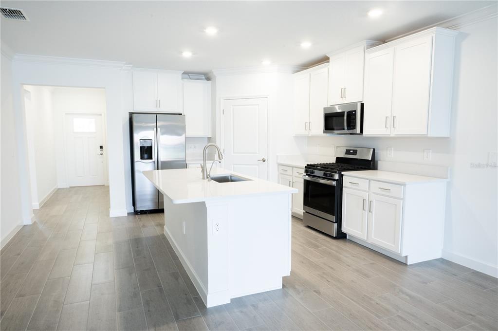 A modern kitchen features white cabinetry, stainless steel appliances, a center island, and gray flooring — 17523 HOLLY WELL AVENUE, WIMAUMA, FL