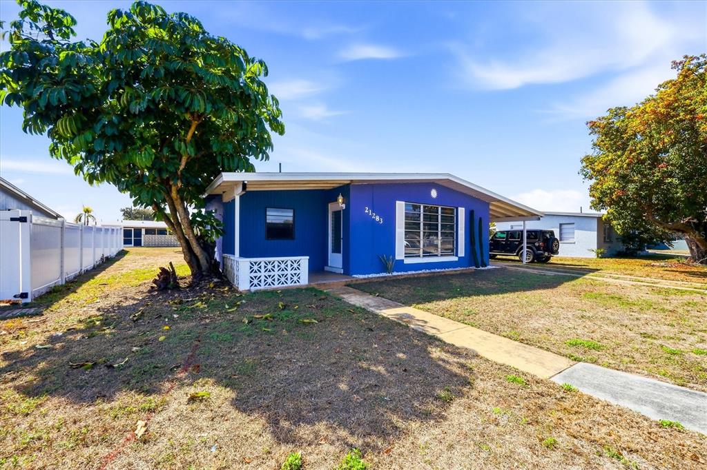 A blue single-story house with a white fence, a large tree, and a driveway — 21283 MIDWAY BOULEVARD, PORT CHARLOTTE, FL