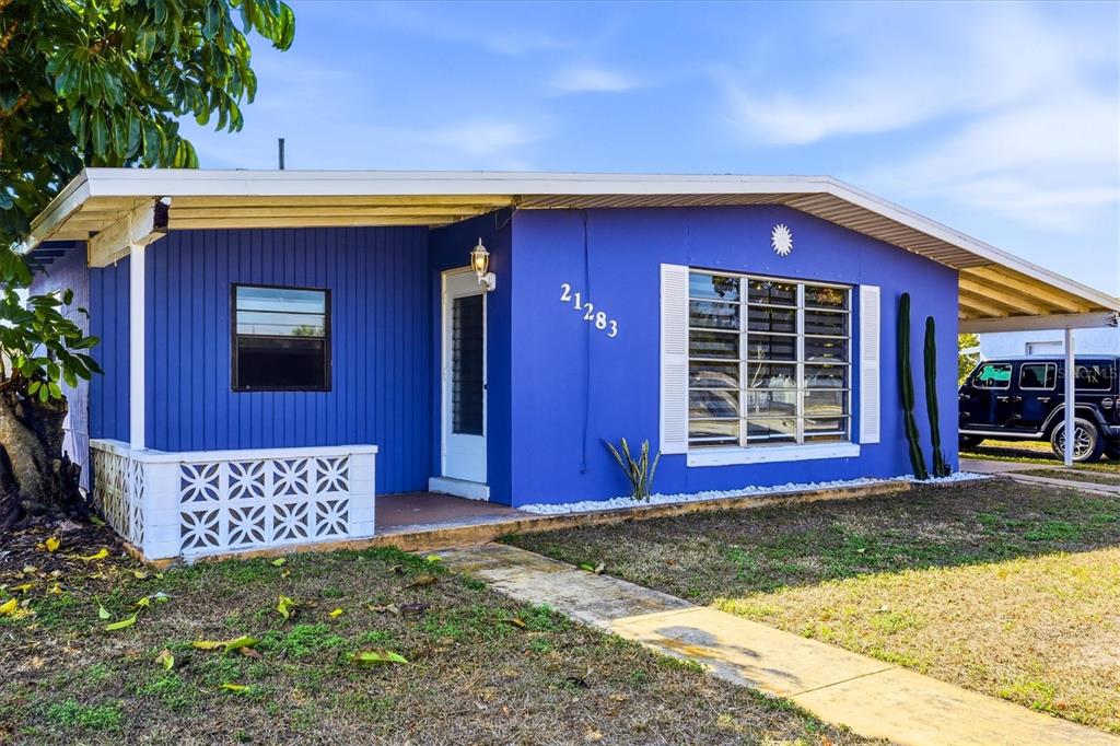 A bright blue single-story house features a white decorative screen wall and a carport — 21283 MIDWAY BOULEVARD, PORT CHARLOTTE, FL