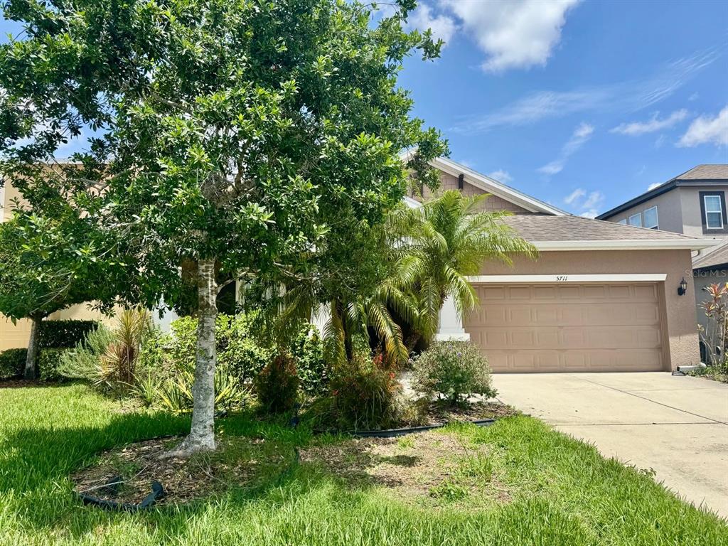 A single-story house with a tan stucco exterior, a two-car garage, and mature landscaping — 5711 ARBOR WOOD COURT, BRADENTON, FL