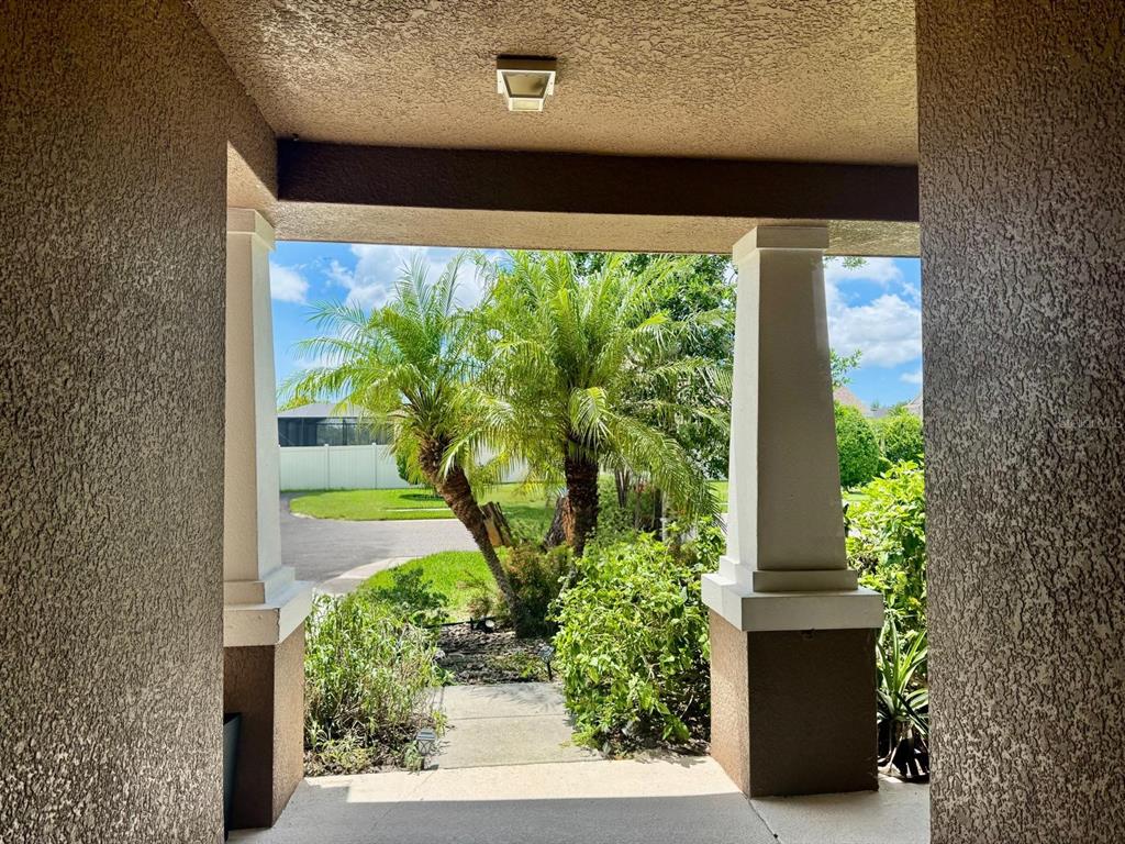 A view from a covered porch looking out toward palm trees and a residential street — 5711 ARBOR WOOD COURT, BRADENTON, FL