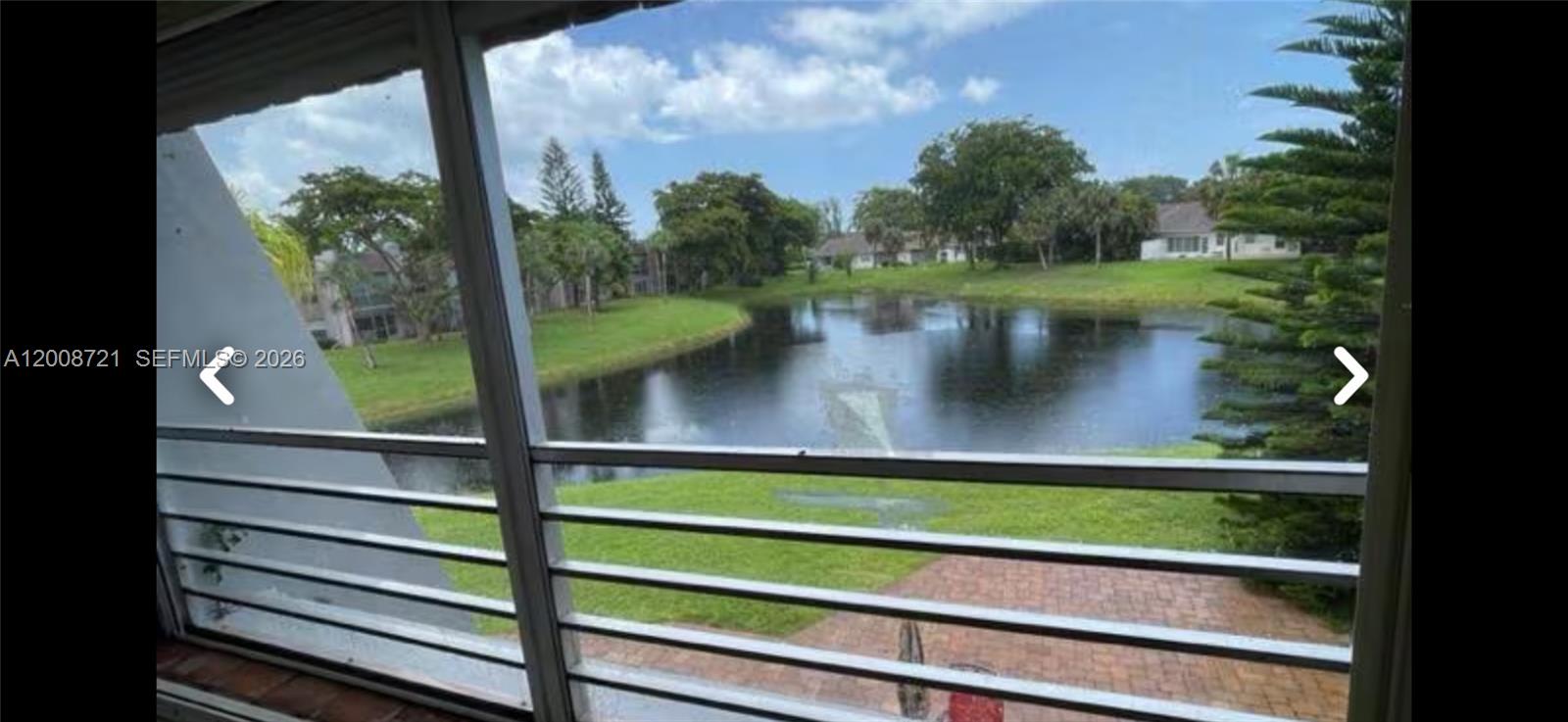 A view of a pond and grassy lawn seen through a window with horizontal blinds — 2600 Fiore Way # B, Delray Beach FL 33445, DELRAY BEACH, FL