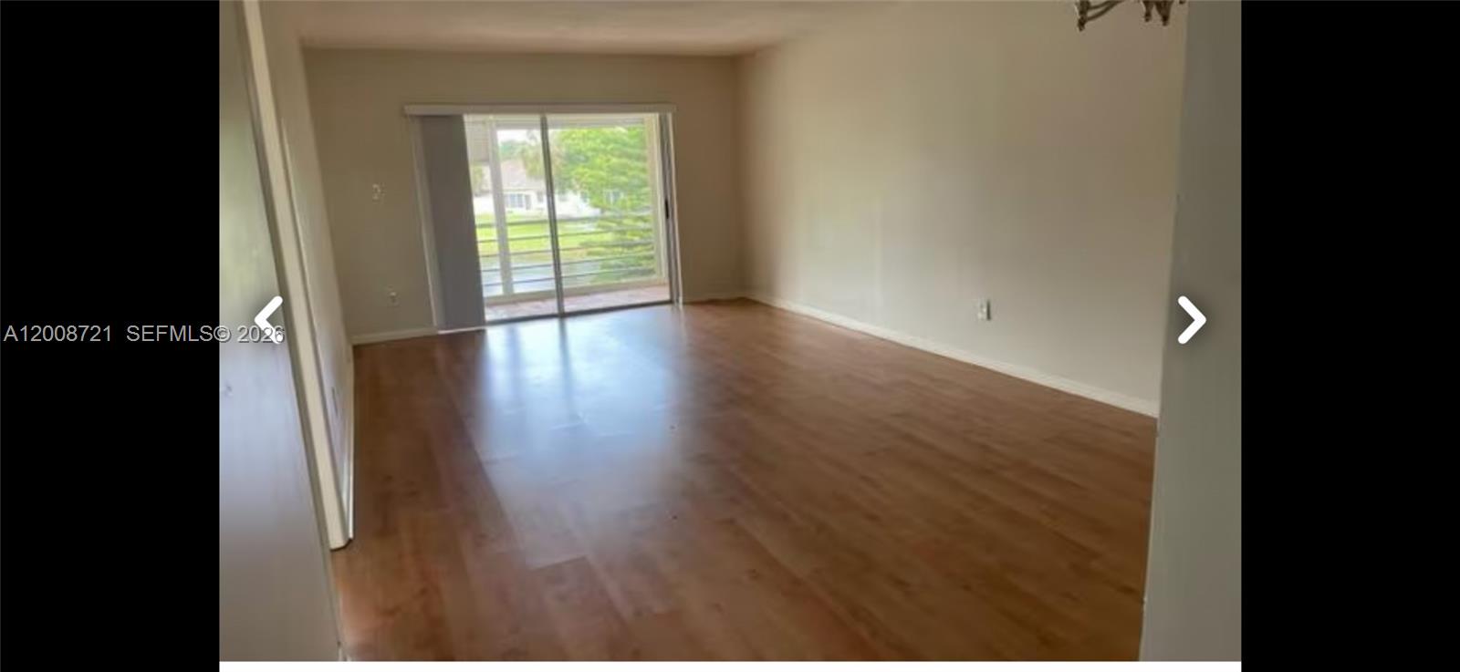 An empty living room features light wood-look flooring and a sliding glass door to a balcony — 2600 Fiore Way # B, Delray Beach FL 33445, DELRAY BEACH, FL