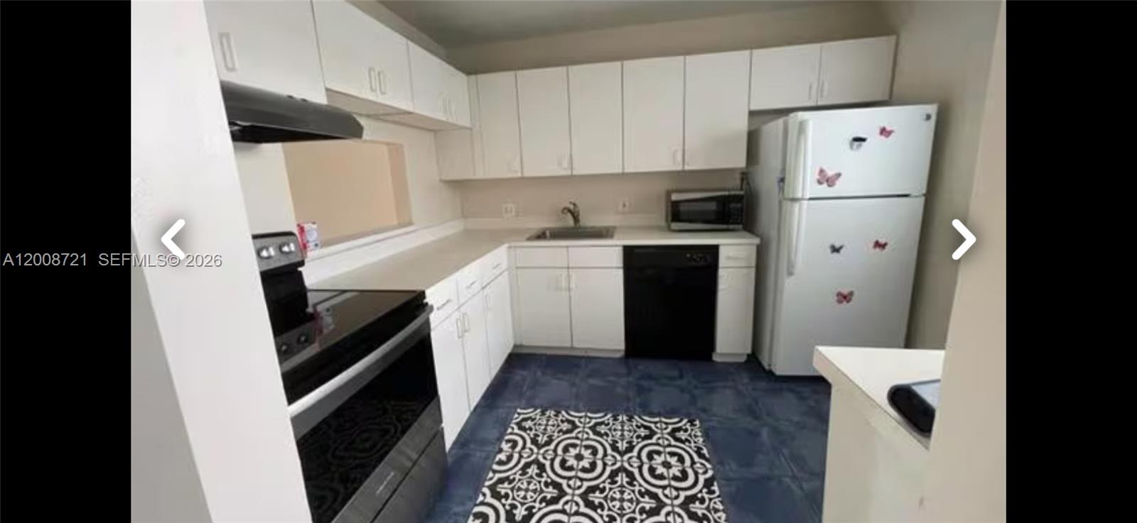 A kitchen features white cabinets, a black dishwasher, a black stove, and patterned floor tiles — 2600 Fiore Way # B, Delray Beach FL 33445, DELRAY BEACH, FL
