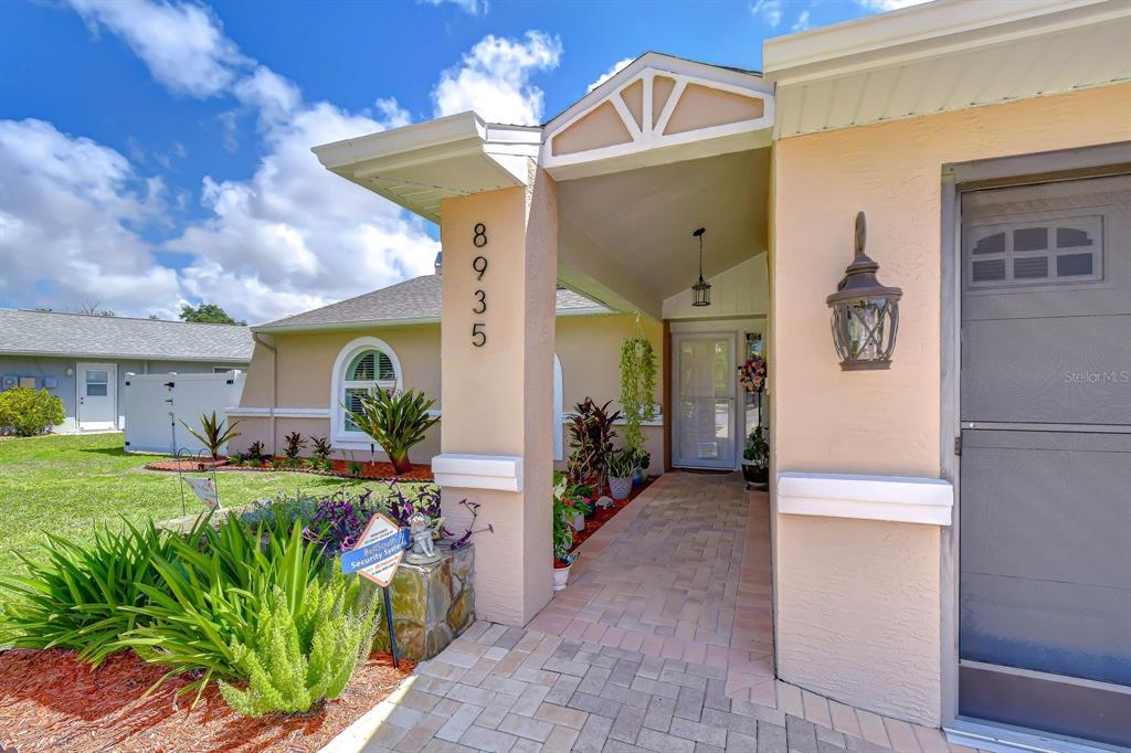 The exterior entrance features a paved walkway, a stone pillar, and a light-colored stucco facade — 8935 RUGER DRIVE, NEW PORT RICHEY, FL