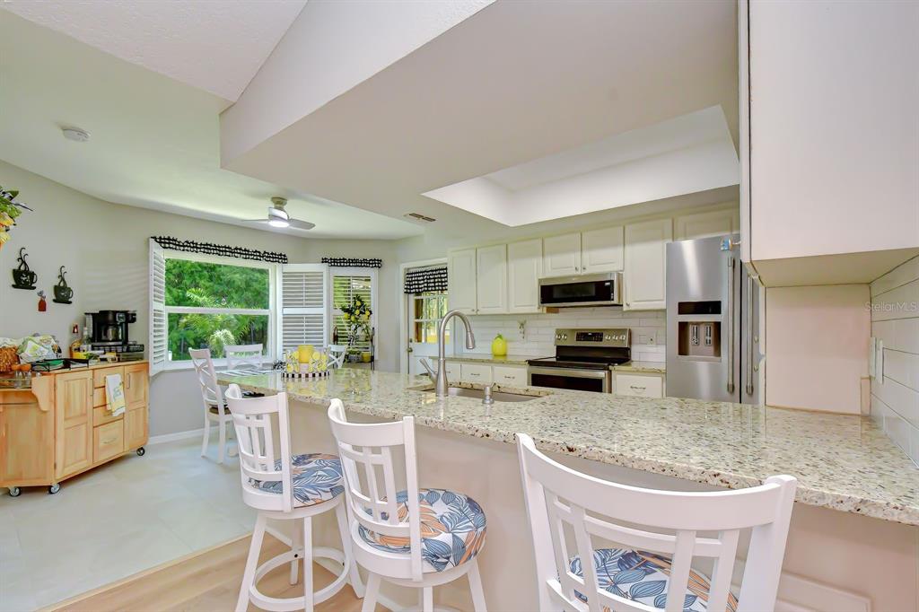 A kitchen with white cabinets, granite countertops, a breakfast bar, and a dining area — 8935 RUGER DRIVE, NEW PORT RICHEY, FL