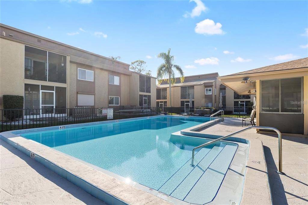 An outdoor swimming pool with steps and a surrounding patio area near apartment buildings — 1589 GREENLEA DRIVE UNIT 3, CLEARWATER, FL