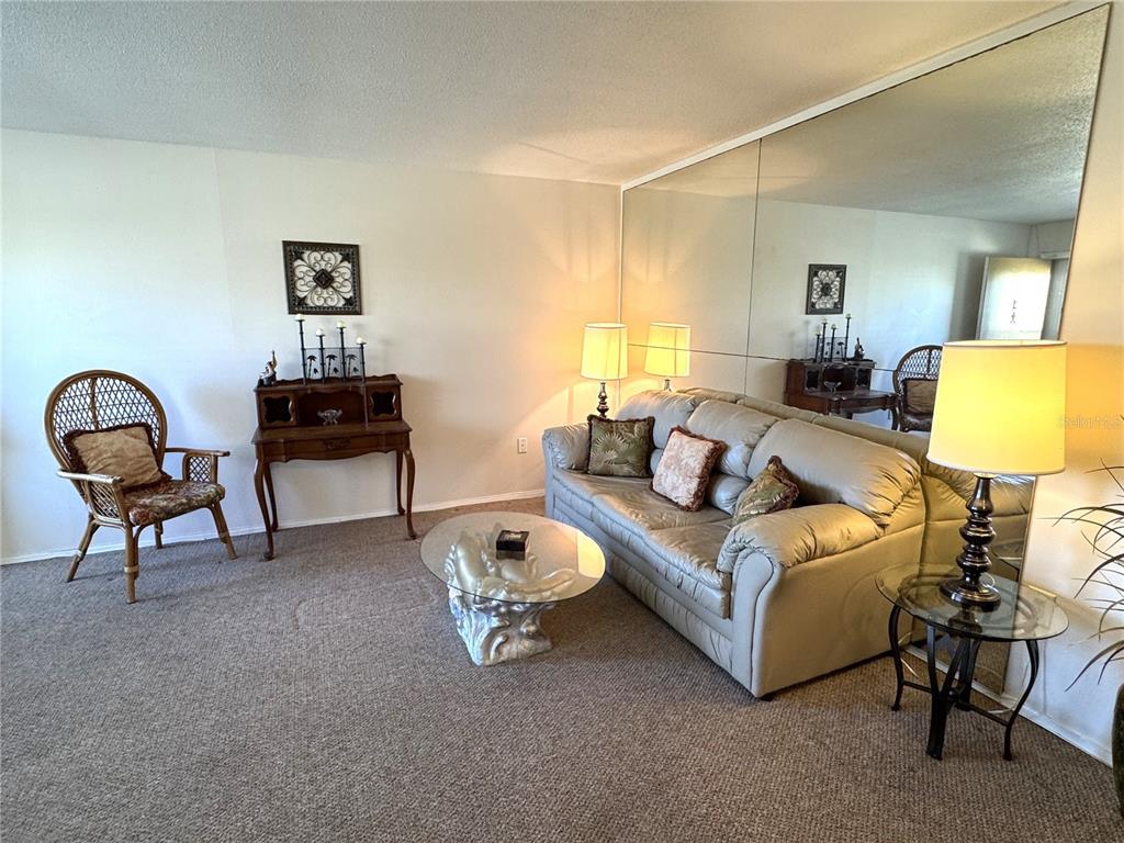 A living room features a beige sofa, a glass coffee table, and a mirrored wall — 4480 IRONWOOD CIRCLE UNIT 308A, BRADENTON, FL