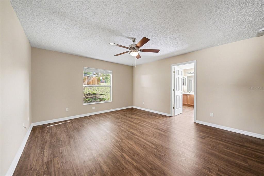 A bedroom features light tan walls, wood-look flooring, a ceiling fan, and an attached bathroom — 1110 BLUEGRASS DRIVE, GROVELAND, FL