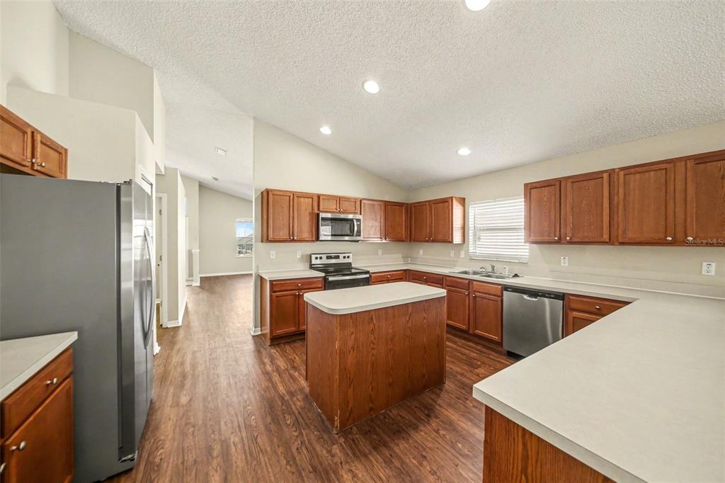 A kitchen features wood cabinets, a central island, stainless steel appliances, and wood-look flooring — 1110 BLUEGRASS DRIVE, GROVELAND, FL