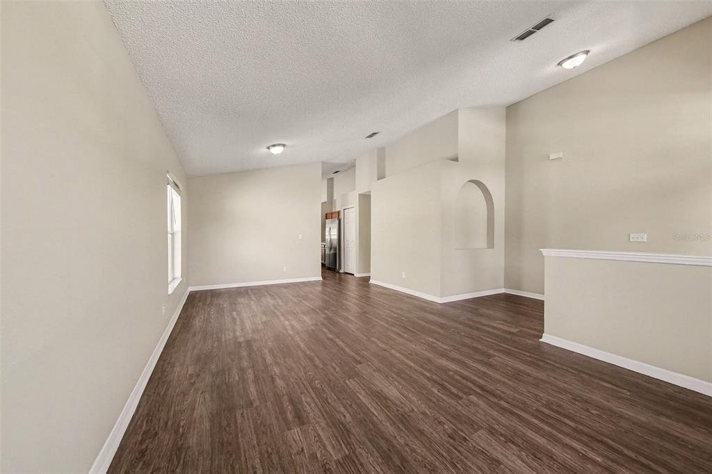 An empty living room with wood-look flooring, vaulted ceilings, and a decorative wall niche — 1110 BLUEGRASS DRIVE, GROVELAND, FL
