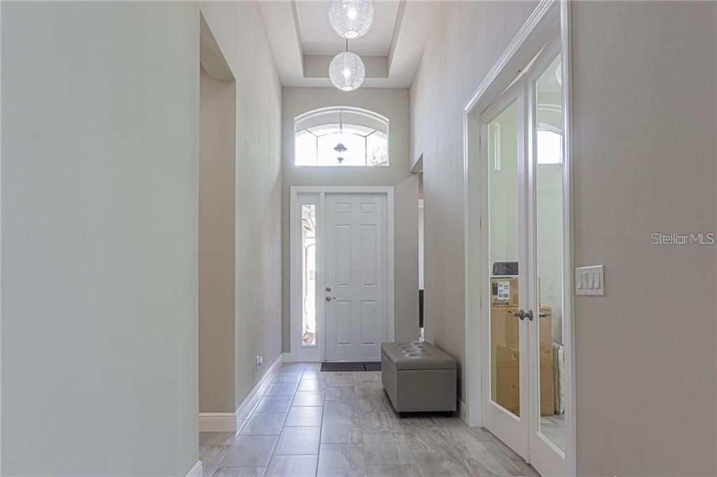 A bright entryway features a tray ceiling, two pendant lights, and a glass-paneled door — 4836 GRAND BANKS DRIVE, WIMAUMA, FL