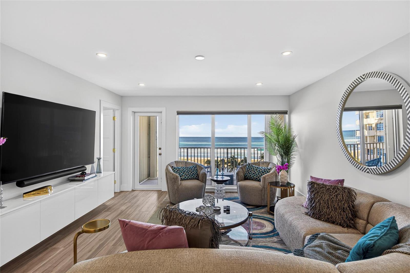 A living room features a large television, curved sofa, two armchairs, and a balcony view — 750 N Ocean Boulevard # 608, Pompano Beach FL 33062, POMPANO BEACH, FL