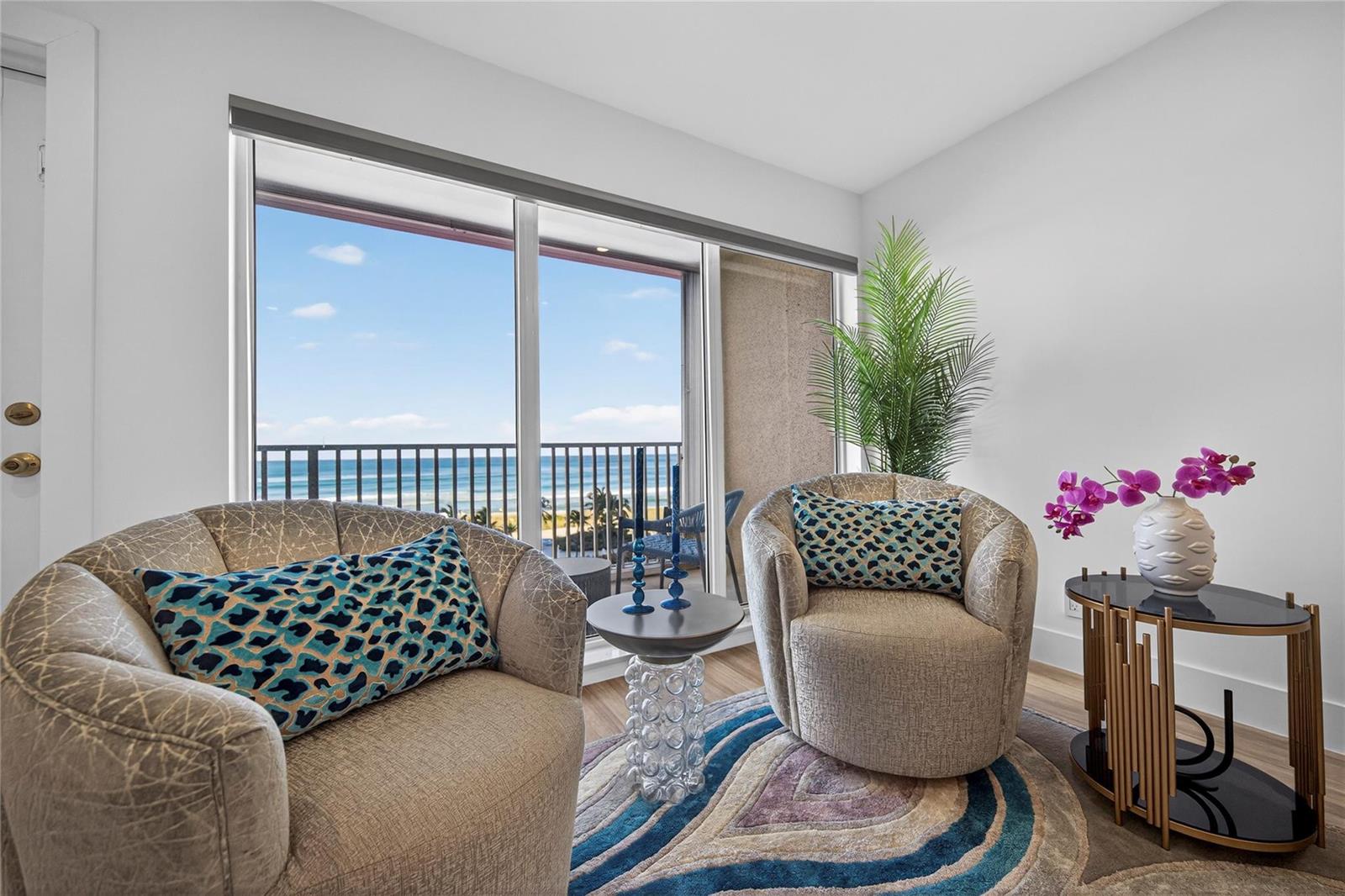 Two armchairs with patterned pillows sit on a circular rug before a balcony ocean view — 750 N Ocean Boulevard # 608, Pompano Beach FL 33062, POMPANO BEACH, FL