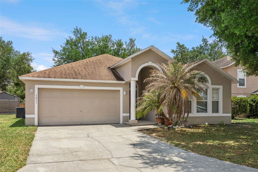 A single-story suburban house with a tan stucco exterior, a two-car garage, and a palm tree — 1871 EMILY DRIVE, WINTER HAVEN, FL