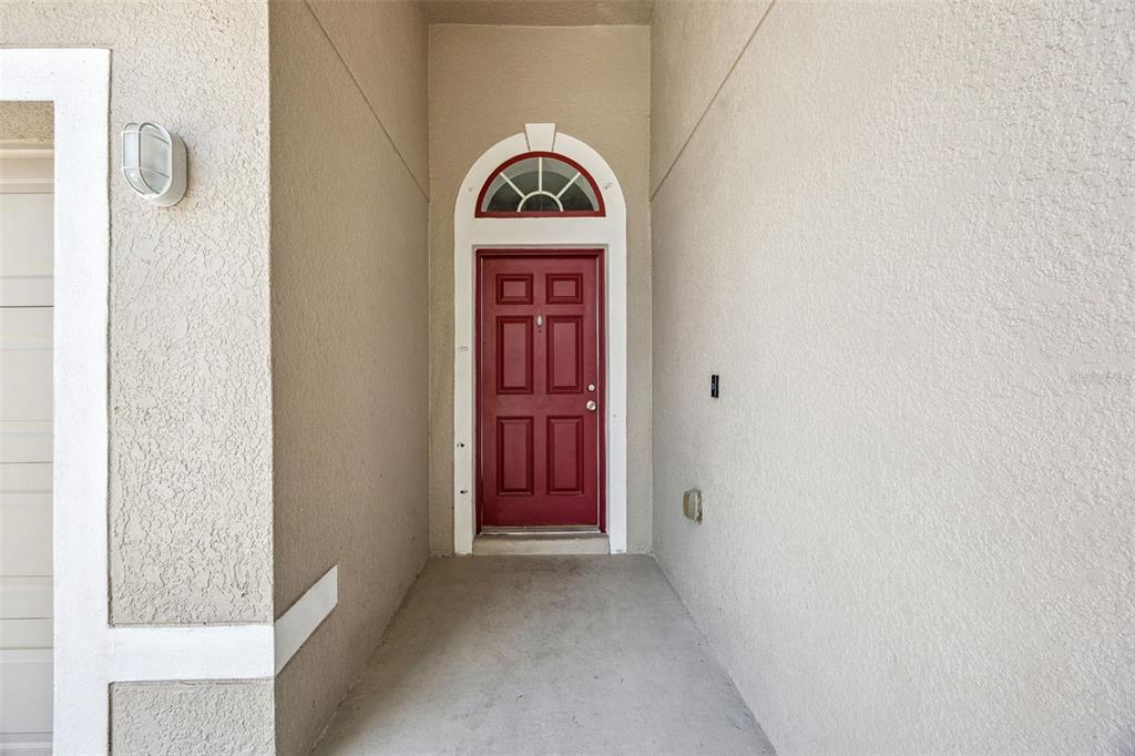 A red front door with an arched transom window sits at the end of a porch — 1871 EMILY DRIVE, WINTER HAVEN, FL