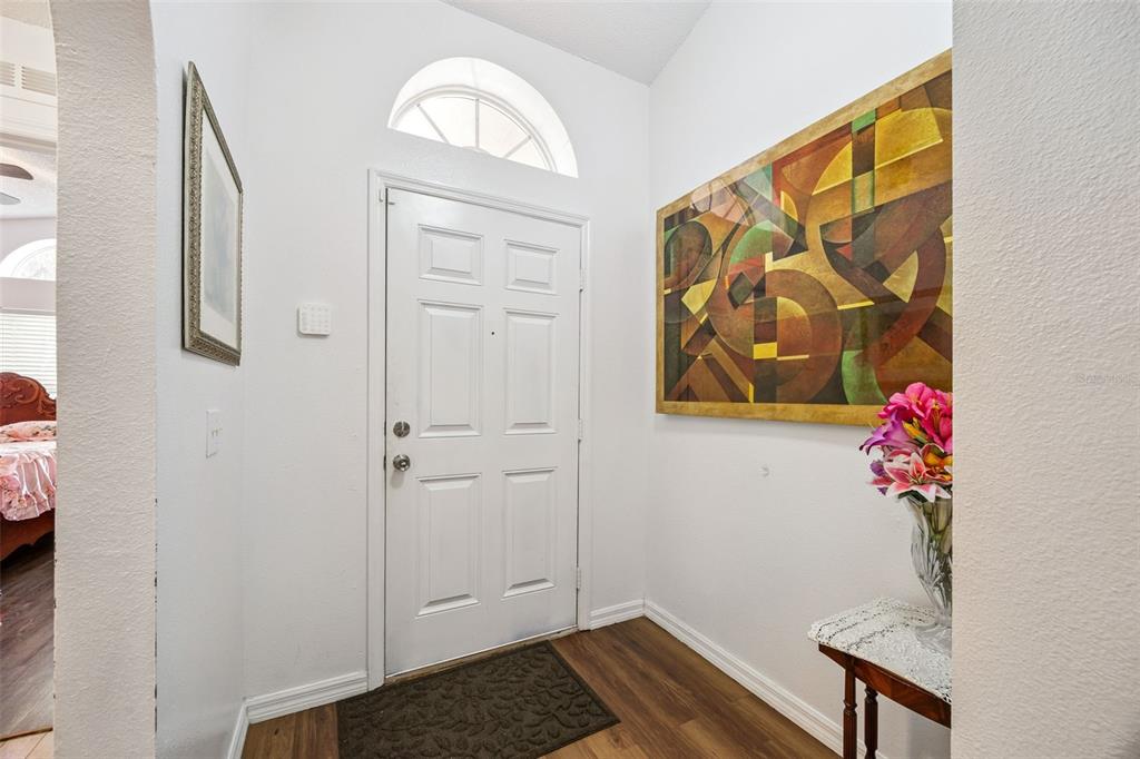 A bright entryway features a white front door, wood-look flooring, and a large abstract painting — 1871 EMILY DRIVE, WINTER HAVEN, FL