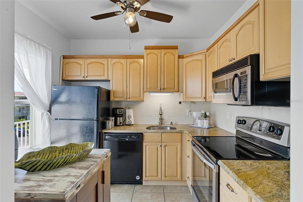 A kitchen features light wood cabinets, black appliances, granite countertops, and a ceiling fan — 715 S BEACH STREET UNIT 314D, DAYTONA BEACH, FL