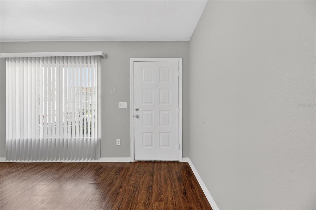A room with wood-look flooring, gray walls, a white front door, and vertical window blinds — 2258 FLUORSHIRE DRIVE, BRANDON, FL