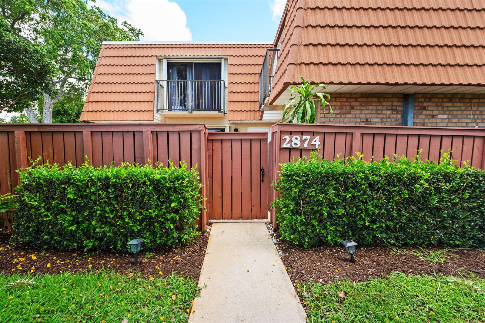 A two-story townhouse exterior features a brown wooden fence, a gate, and a balcony — 2874 Waterford Drive S, Deerfield Beach FL 33442, DEERFIELD BEACH, FL