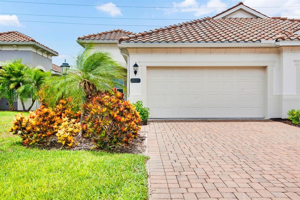 A beige house with a tiled roof, a two-car garage, and a brick paver driveway — 1418 CALLE GRAND STREET, BRADENTON, FL