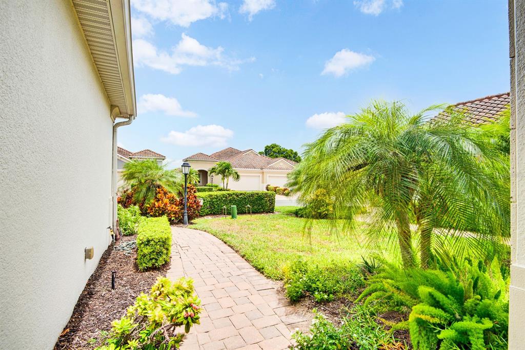 A paved walkway leads through a landscaped yard toward neighboring houses under a blue sky — 1418 CALLE GRAND STREET, BRADENTON, FL