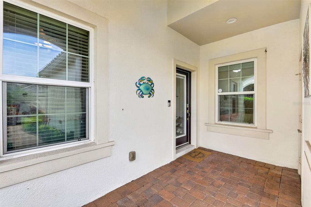 A covered front porch features a black metal bench, a potted plant, and a door — 1418 CALLE GRAND STREET, BRADENTON, FL