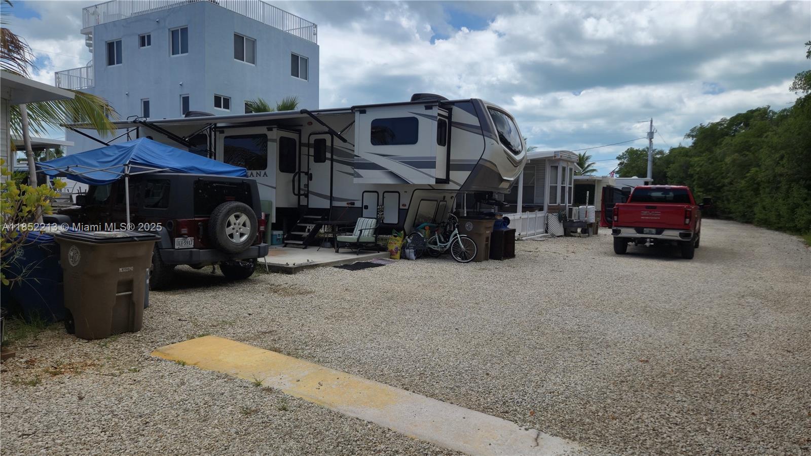 A gravel lot features a parked fifth-wheel RV, a Jeep, and a red pickup truck — 325 Calusa St lot 333, Key Largo FL 33037, KEY LARGO, FL