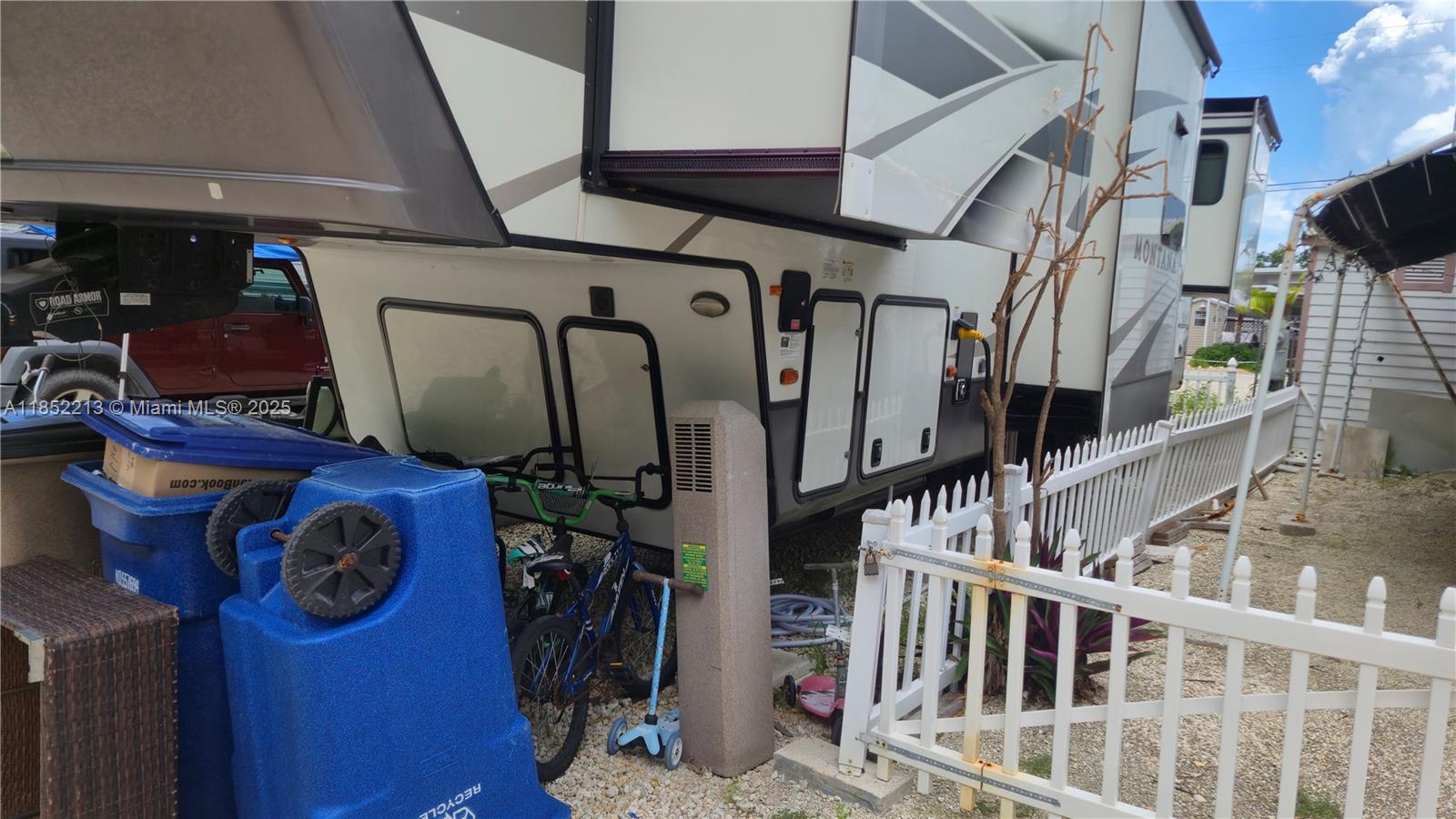 A large recreational vehicle is parked next to a white fence and blue recycling bins — 325 Calusa St lot 333, Key Largo FL 33037, KEY LARGO, FL
