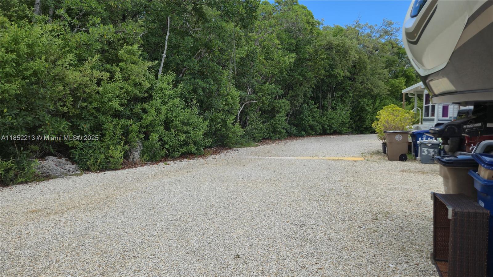 A gravel driveway leads toward a dense line of trees next to a parked RV — 325 Calusa St lot 333, Key Largo FL 33037, KEY LARGO, FL