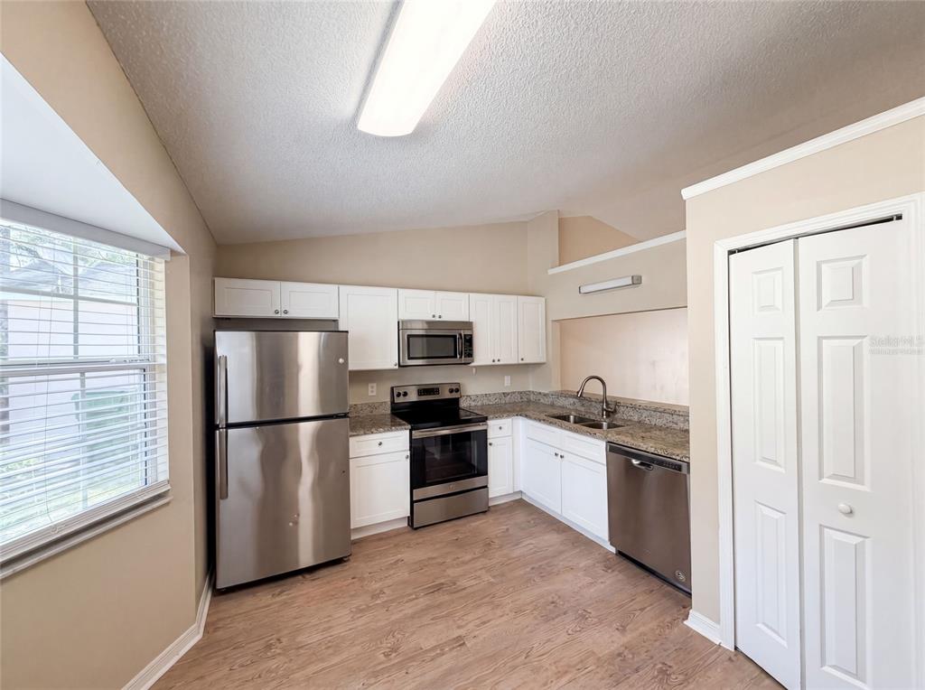 A kitchen features stainless steel appliances, white cabinets, granite countertops, and wood-look flooring — 2715 LORRAINE DRIVE, LEESBURG, FL
