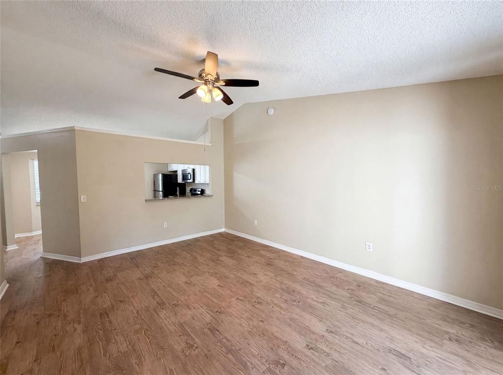 An empty living room features wood-look flooring, a ceiling fan, and a kitchen pass-through window — 2715 LORRAINE DRIVE, LEESBURG, FL